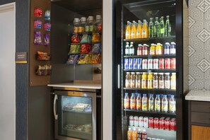 A refrigerated display case with various beverages and snacks, a freezer with frozen goods, and a wall-mounted pegboard with packaged items. - Aiden Sacramento Downtown (Sacramento)
