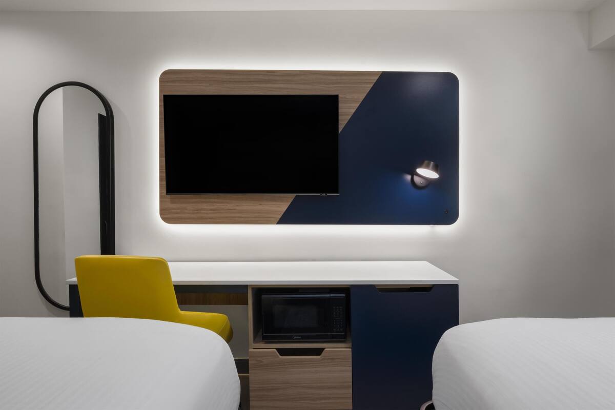 A modern hotel room with a flat-screen TV, a microwave, a desk, and two beds.