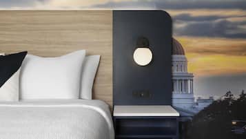 A bed with white bedding, a nightstand with a wall-mounted light, and a view of a building with a dome.