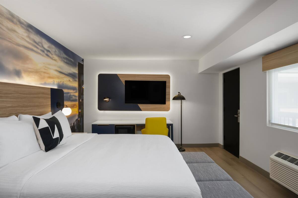 A modern hotel room with a large bed, a desk, a chair, a TV, and a window.