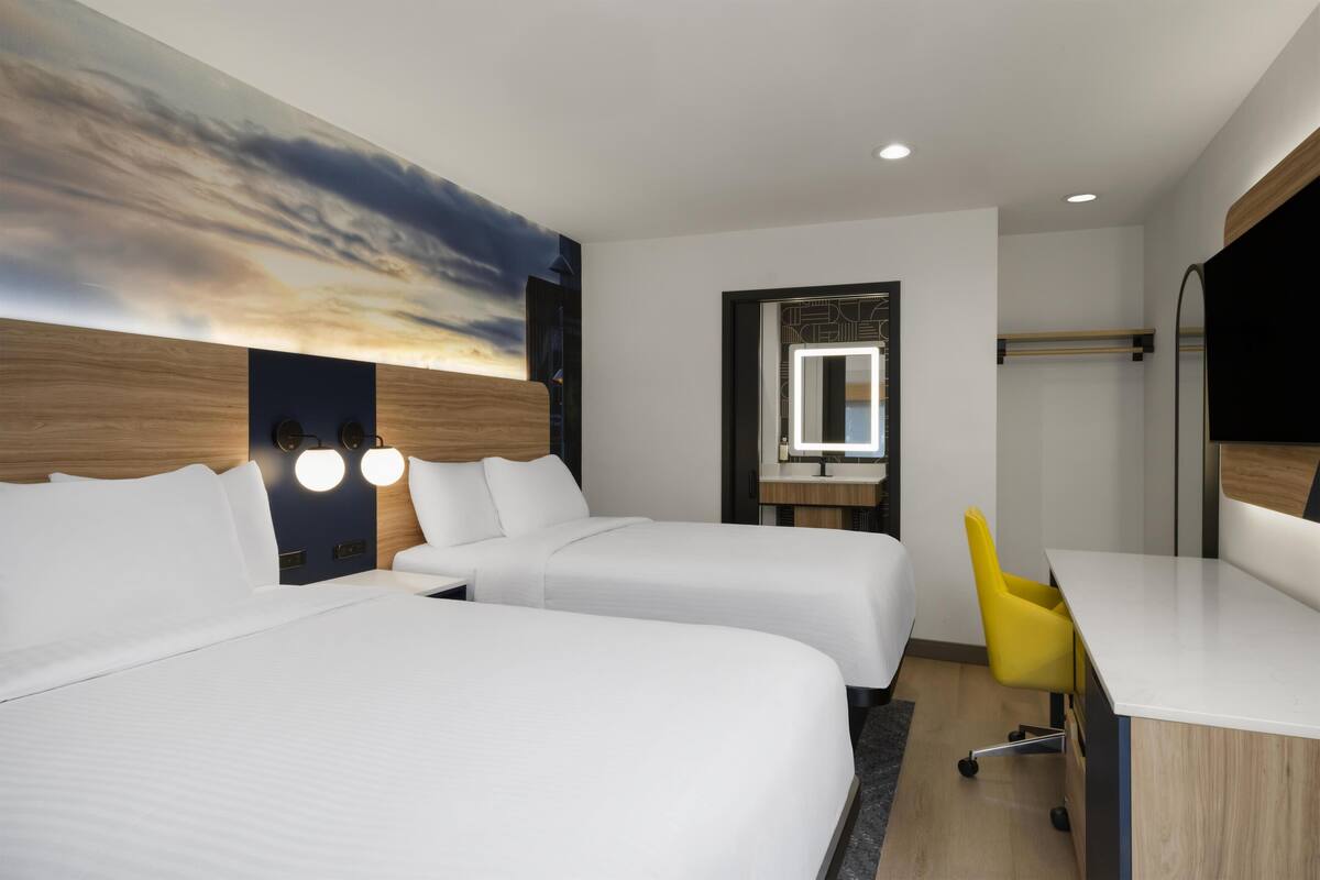 A hotel room with two beds, a desk, a chair, a large painting, and a mirror.