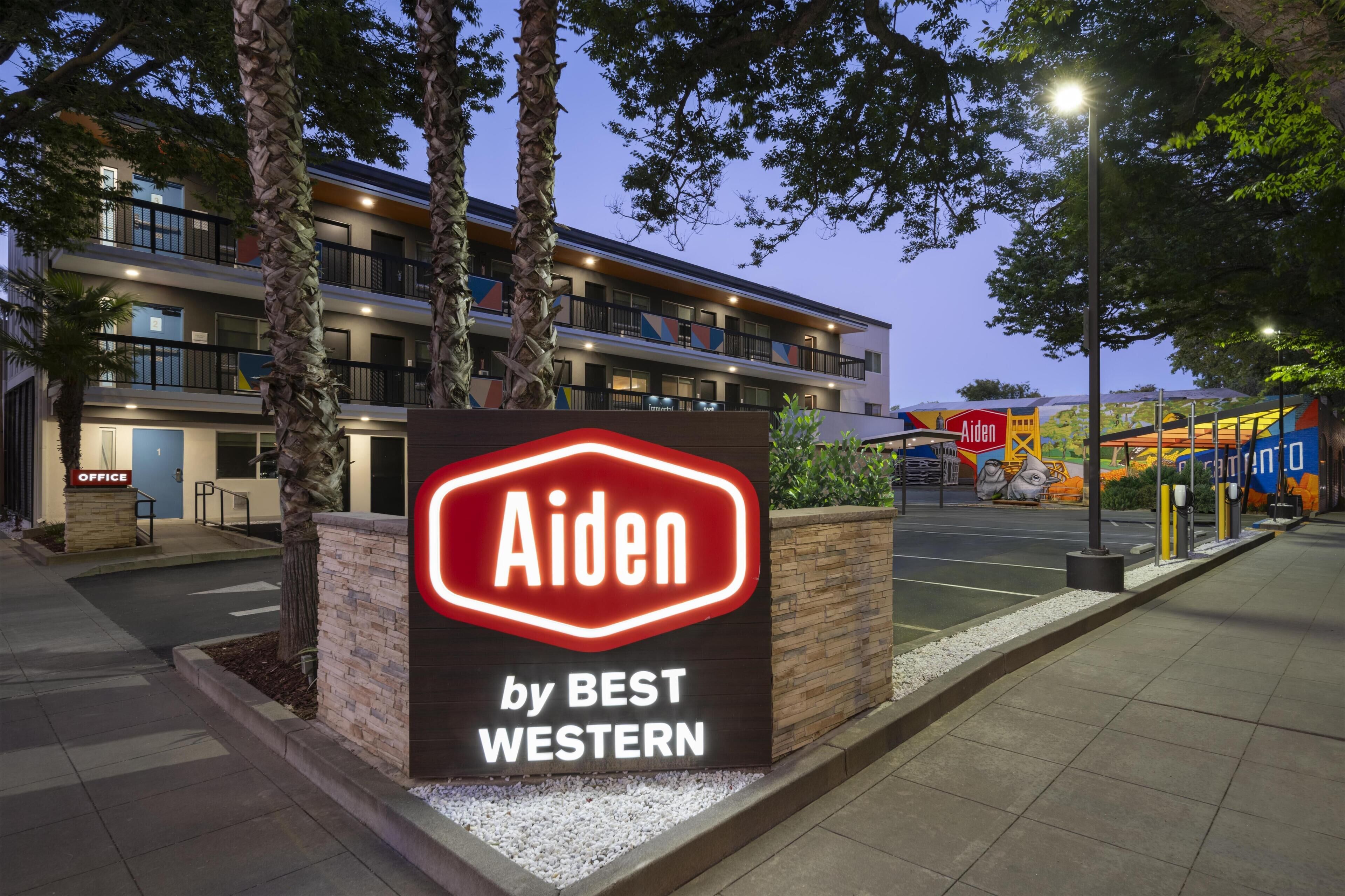 A hotel sign with 'Aiden by BEST WESTERN' illuminated in red neon.