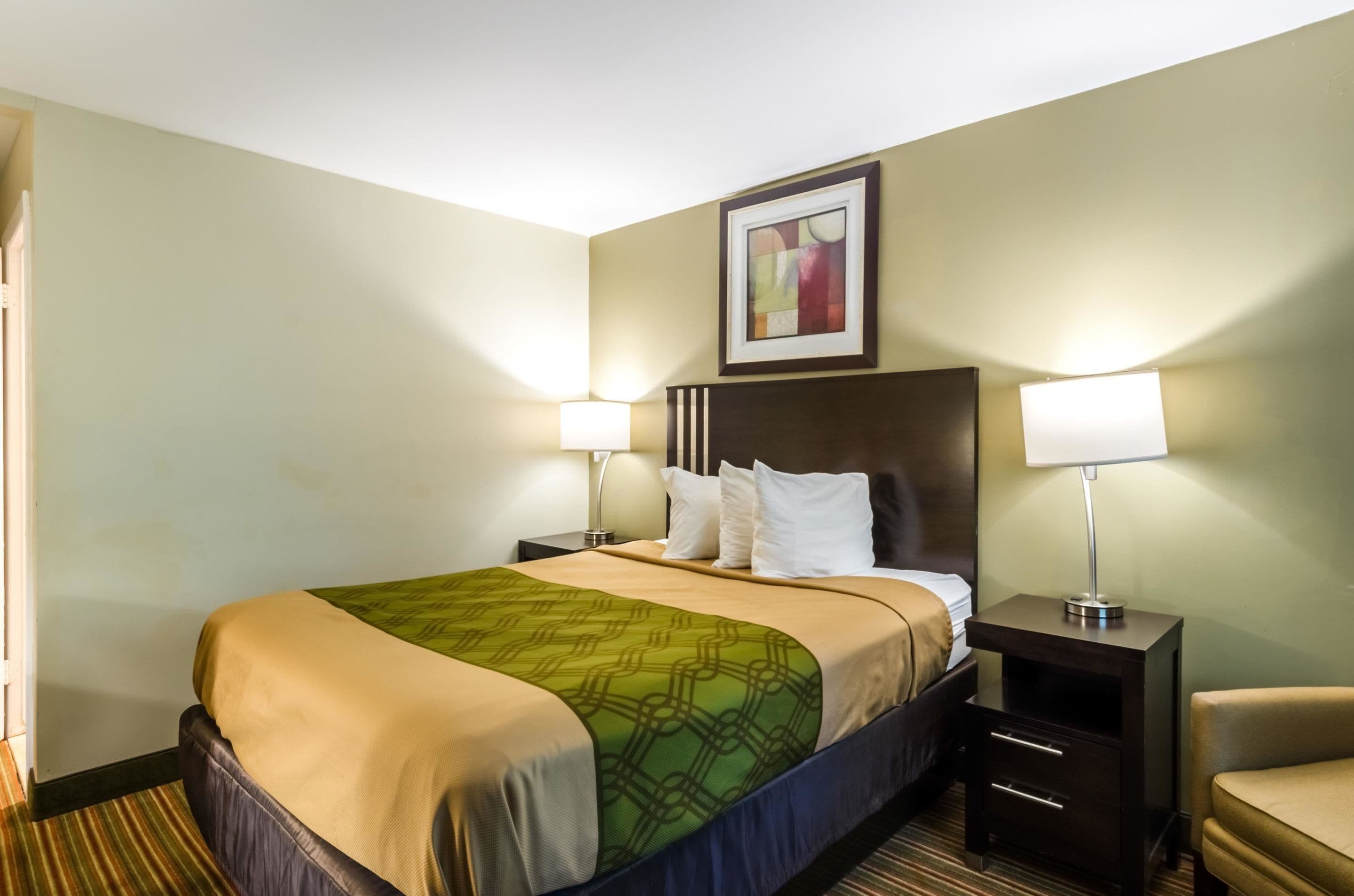 A hotel room with a large bed, two bedside tables with lamps, a chair, and a painting on the wall.