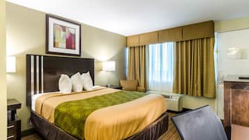 Hotelkamer met een groot bed, een bureau, een stoel, een bureaulamp, een foto aan de muur en een raam met gordijnen.