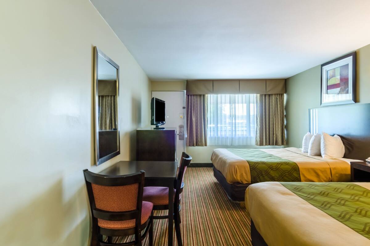 Een hotelkamer met een bed, een bureau met stoel, een televisie en een raam met gordijnen.