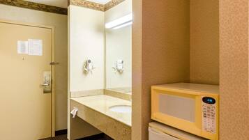 Un baño de hotel con lavamanos, espejo, secador de pelo y microondas.