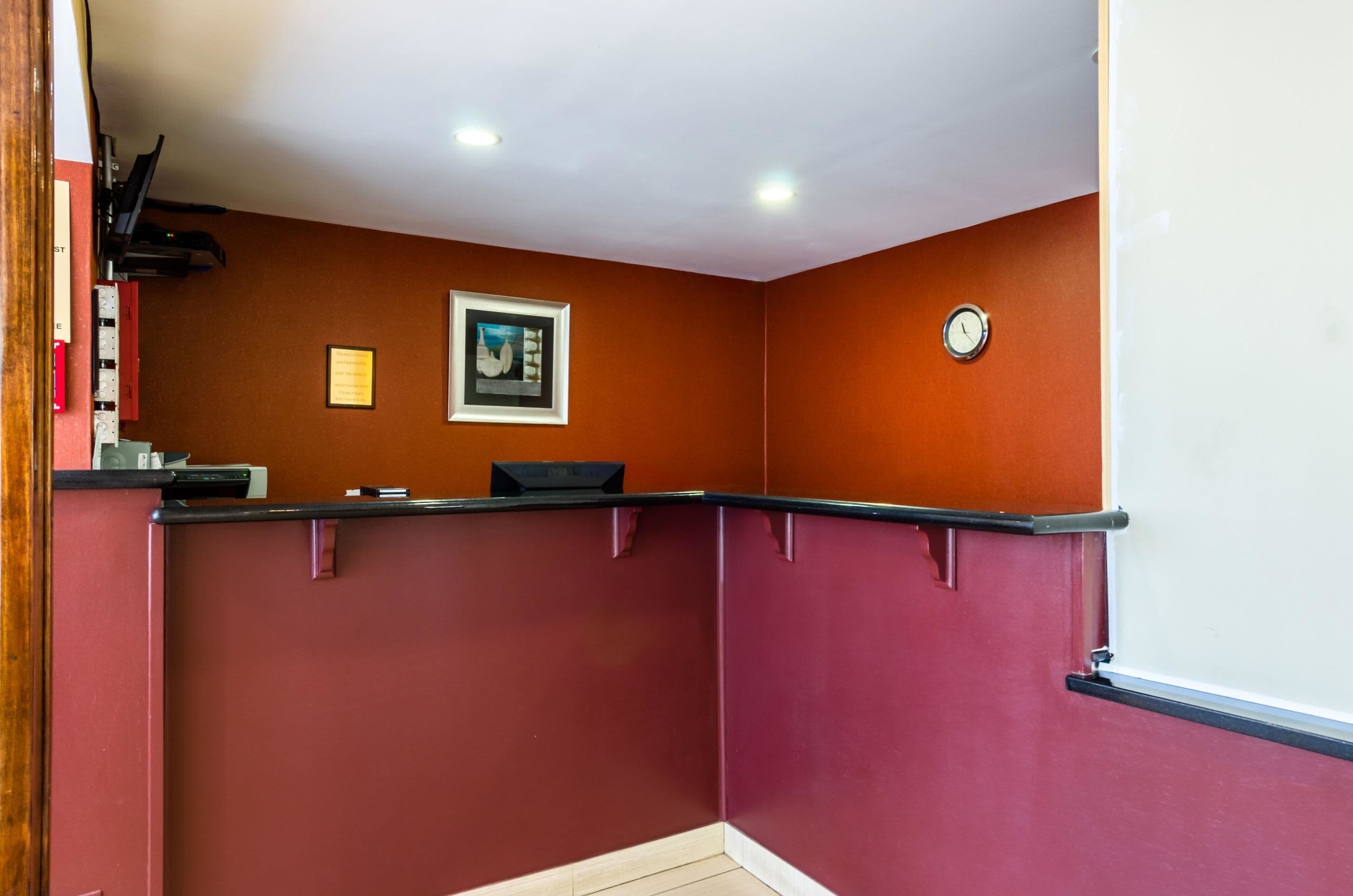 A room with a red wall, a black counter, a framed picture, and a clock on the wall.