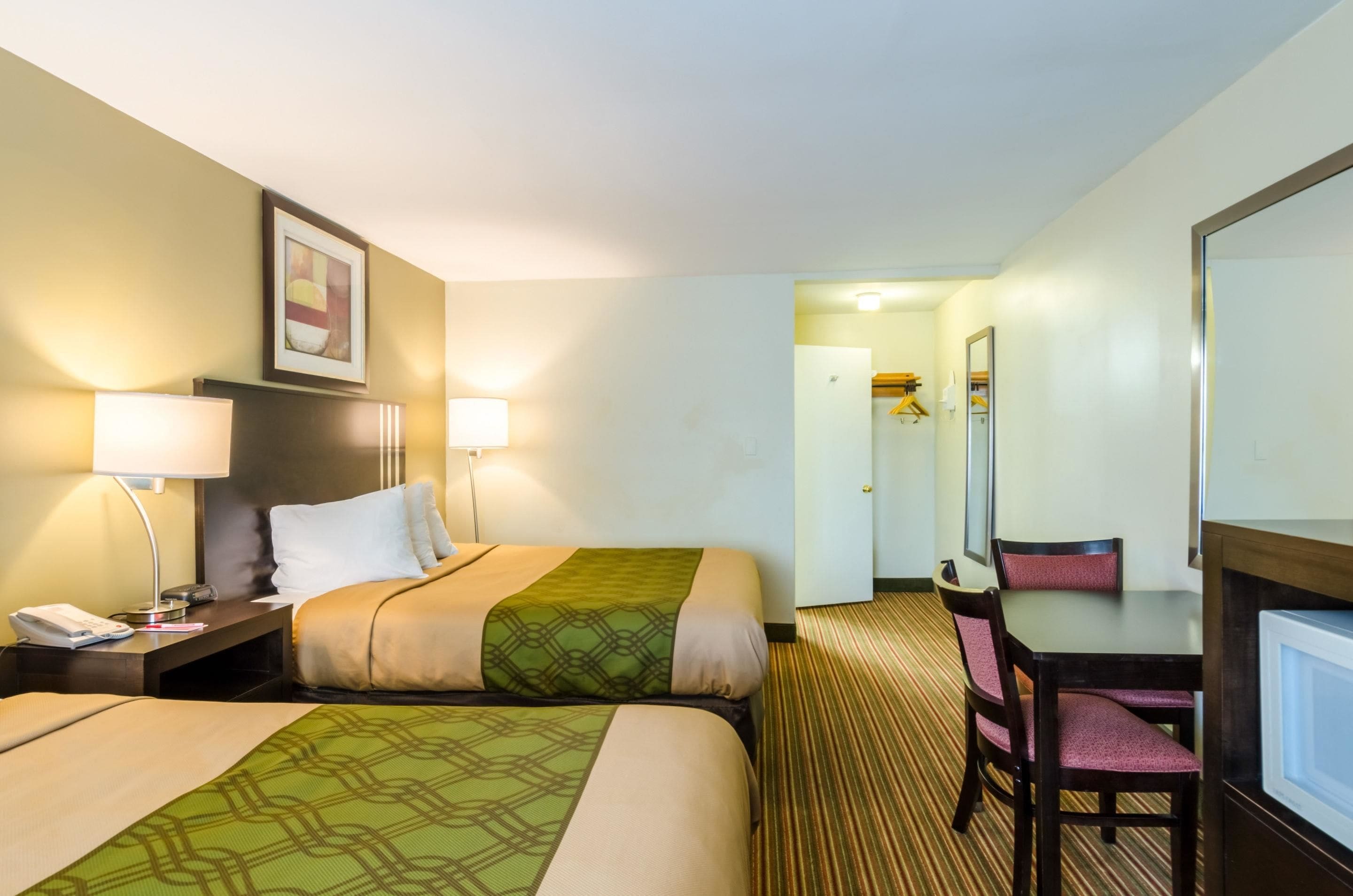 A hotel room with two beds, a desk, a chair, and a mirror.