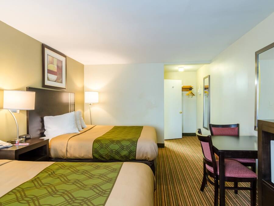 A hotel room with two beds, a desk, a chair, and a mirror.