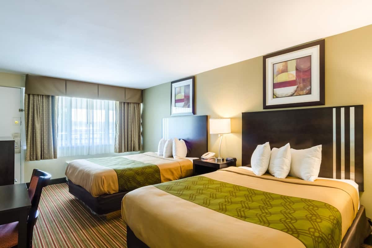 Een hotelkamer met twee bedden, een bureau, een stoel, een lamp en een schilderij aan de muur.