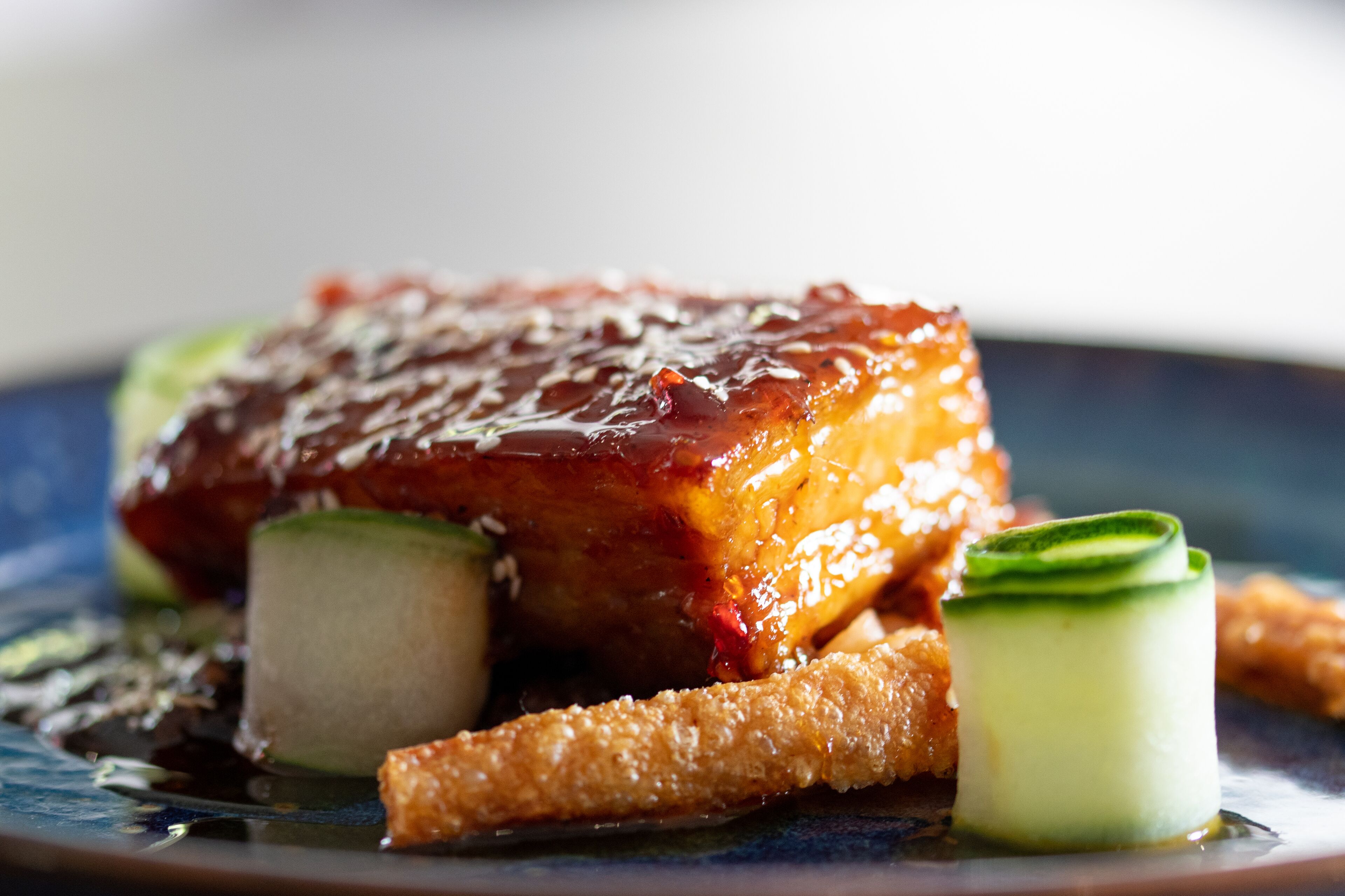 Un plat composé de viande laquée, de légumes et d’éléments croustillants, le tout présenté dans une assiette.