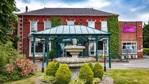 A brick building with a green-roofed pavilion and a stone fountain. - Parkmore Hotel & Leisure Club, Sure Hotel Collection by BW (Stockton-on-Tees)