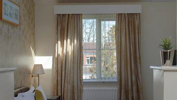 Ein Schlafzimmer mit Oberlicht, einem Bett, einem Nachttisch, einer Lampe und einem Fenster mit Vorhängen.