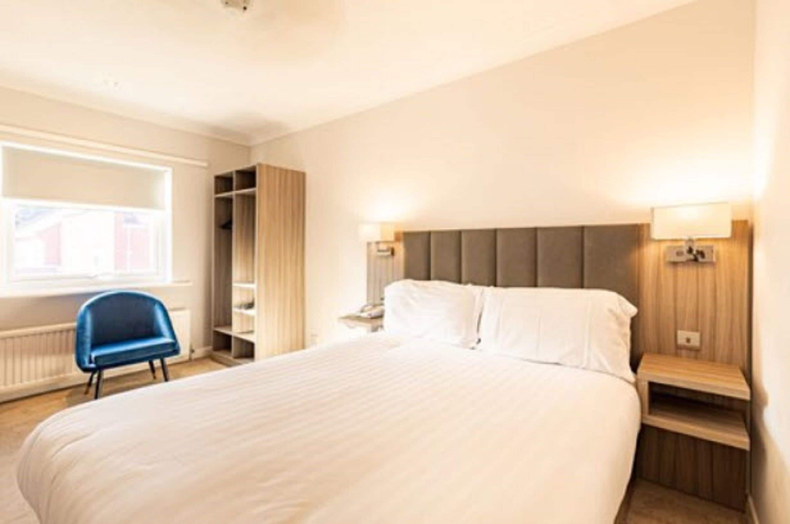 A hotel room with a large bed, bedside lamps, a wardrobe, and a window with blinds.
