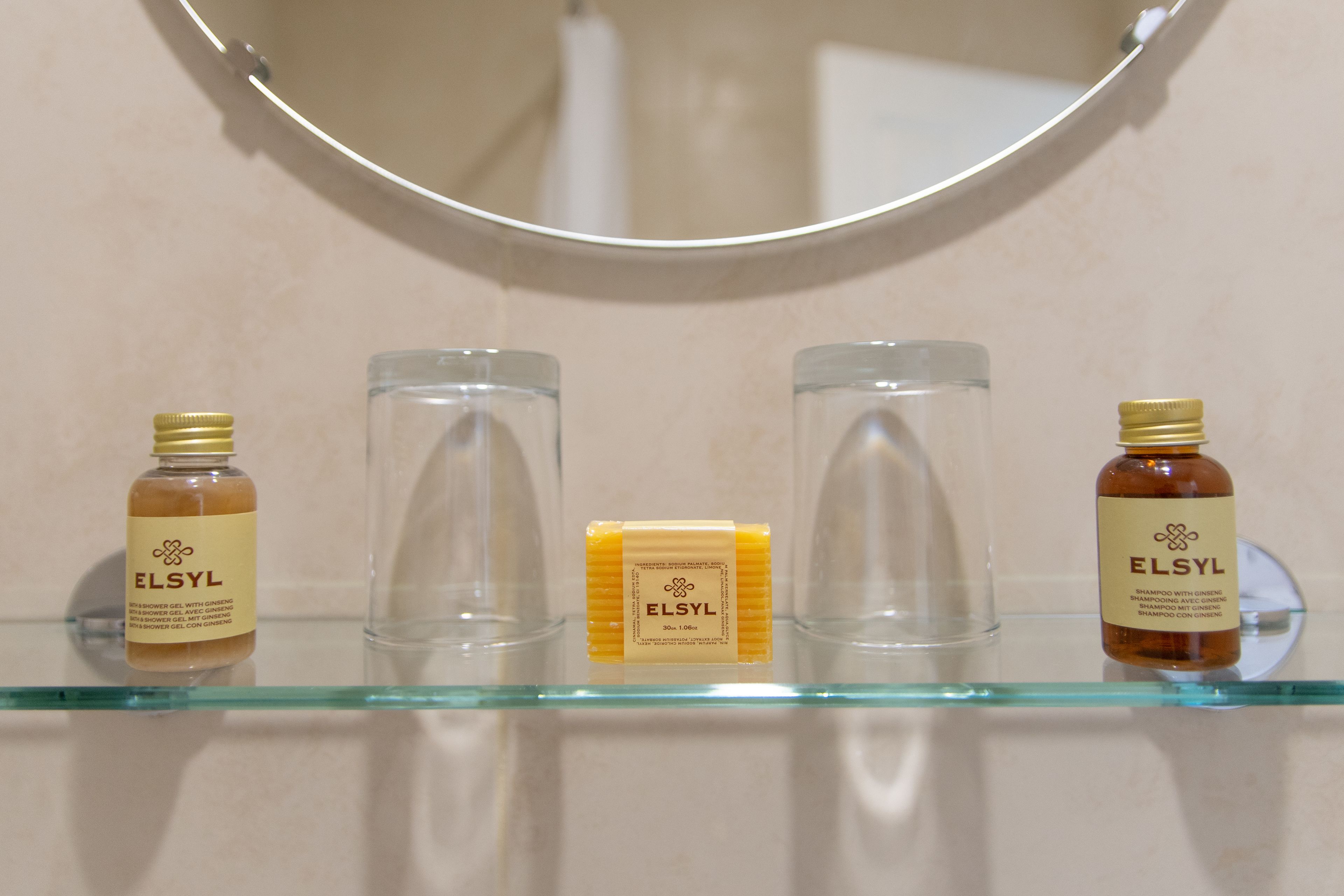 A bathroom shelf with three ELSYL products: a shower gel, a bar of soap, and a shampoo bottle.