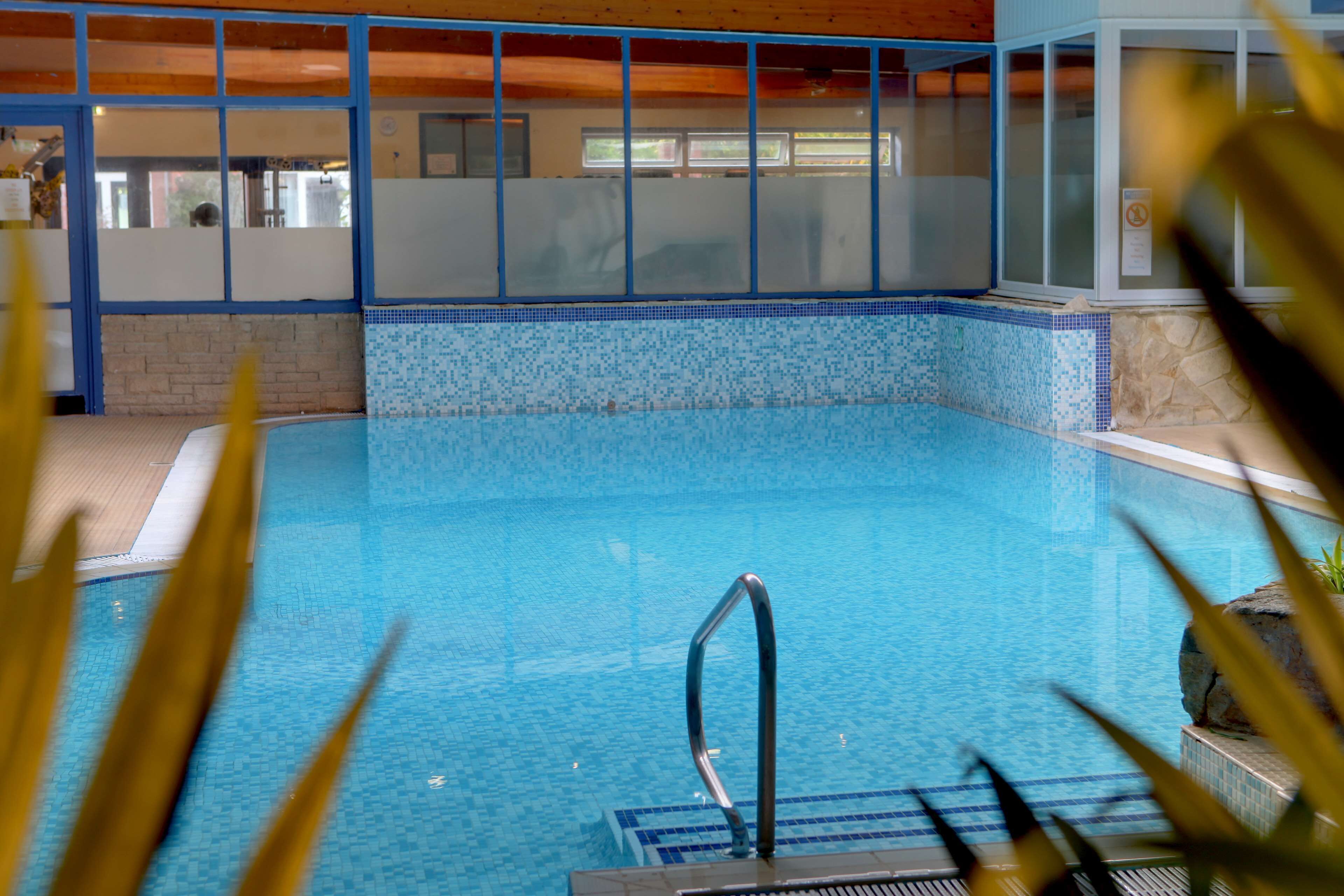Piscina interior com água azul cristalina, escada de metal e borda revestida de azulejos.