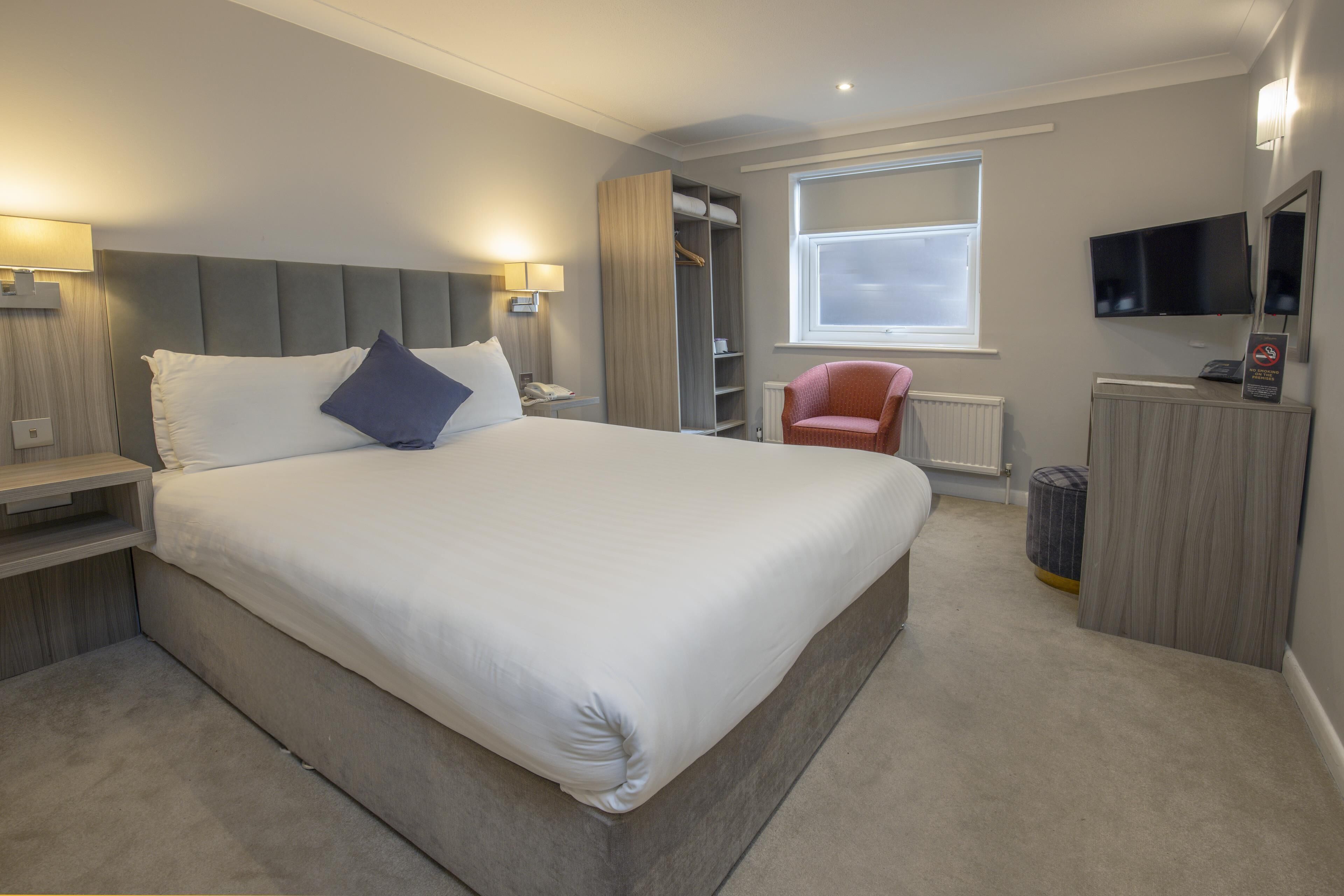 A modern hotel room with a large bed, bedside tables, a wardrobe, a television, and a window.