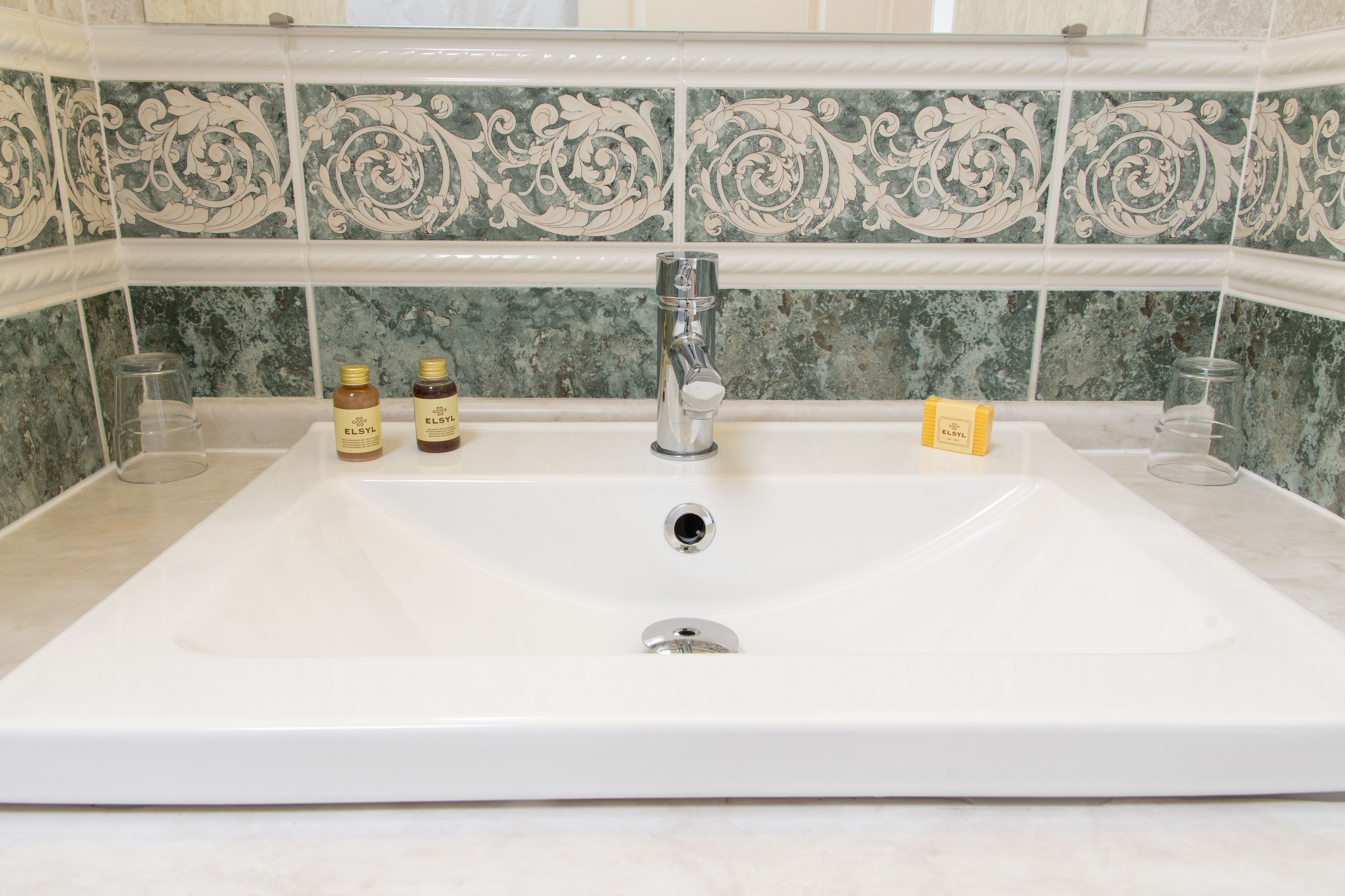 A bathroom with a large sink, a mirror, and decorative tiles.