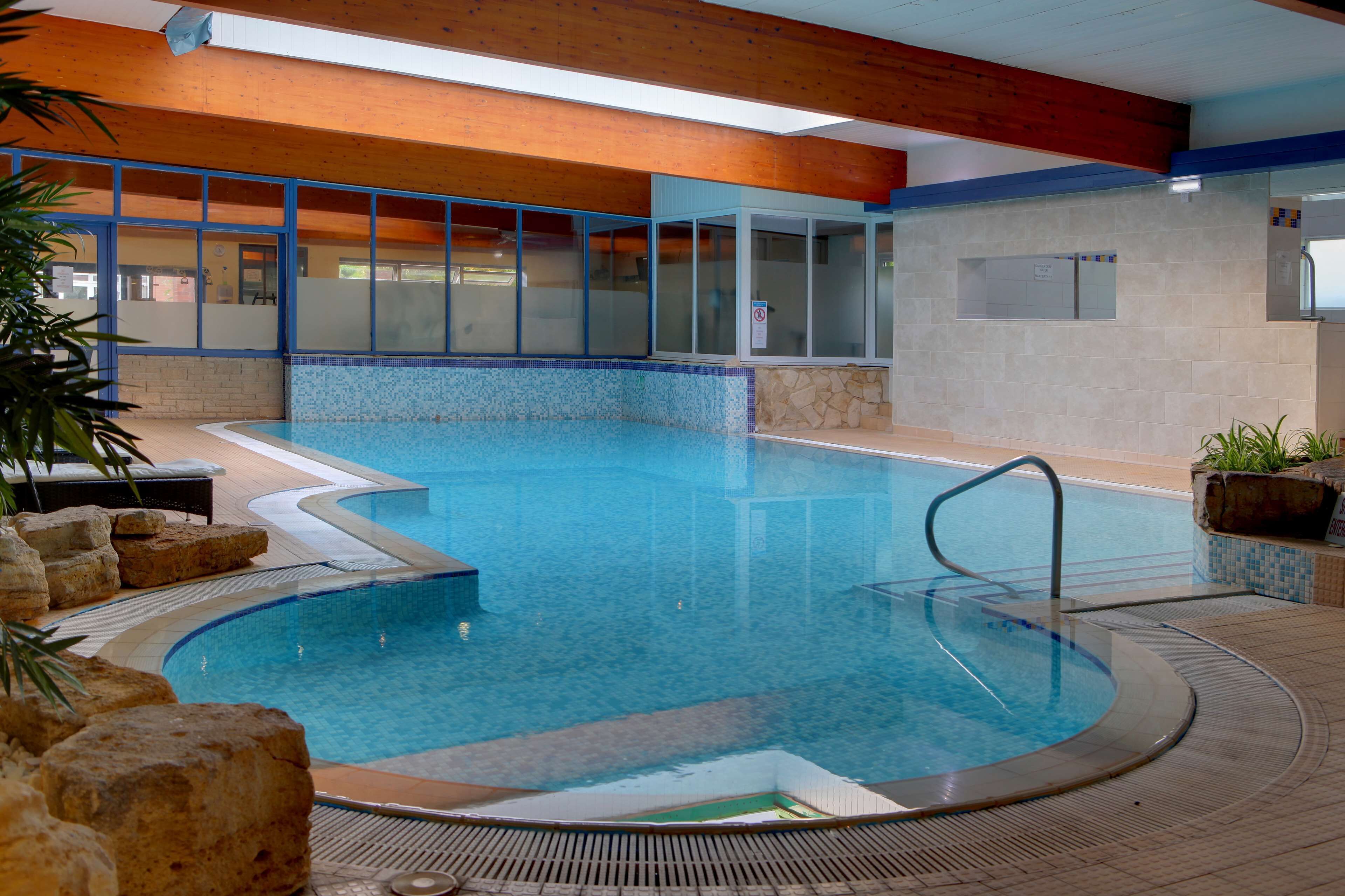 An indoor swimming pool with clear water, surrounded by lounge chairs and a stone wall.