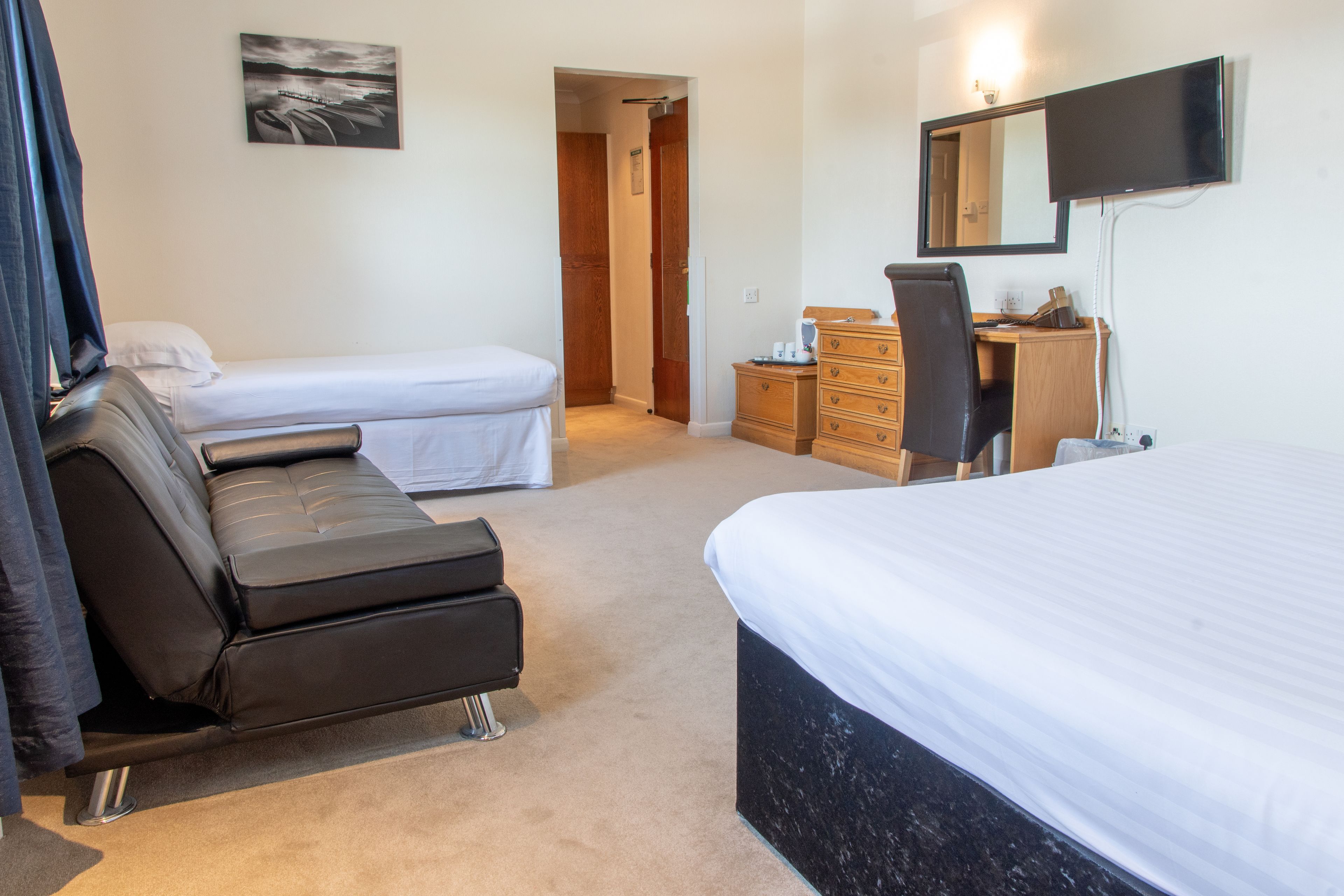 A hotel room with a large bed, a smaller bed, a sofa, a dresser, a desk, and a TV.