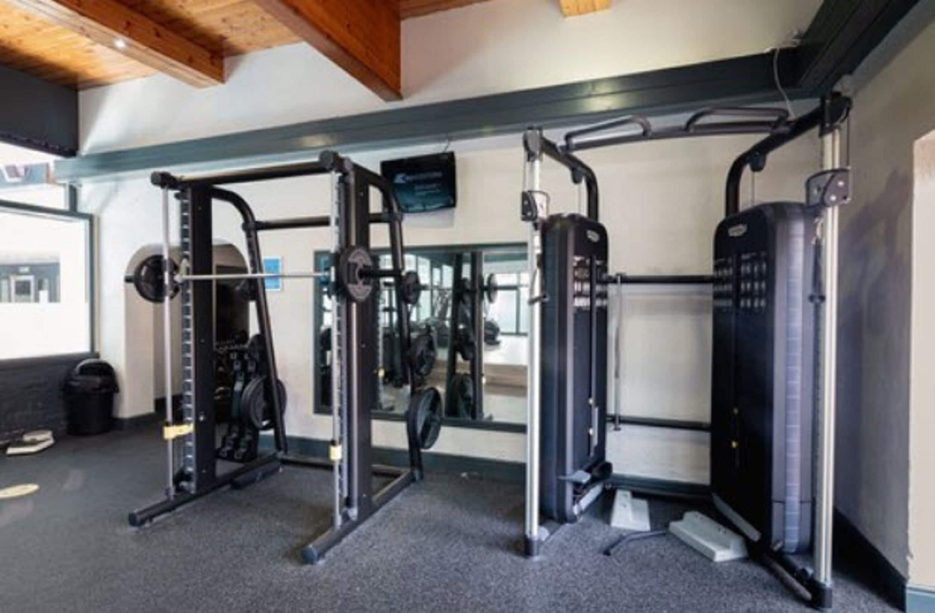 A gym with weightlifting equipment, a mirror, and a television on the wall.