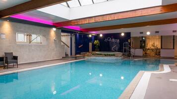 Una piscina interior con vista despejada al techo, un área de spa y una recepción.