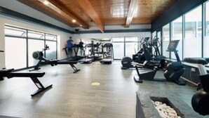 Een sportschool met diverse fitnessapparaten, grote ramen en een houten plafond.