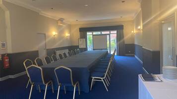 Une salle de conférence avec une longue table, des rangées de chaises et un écran de projection.