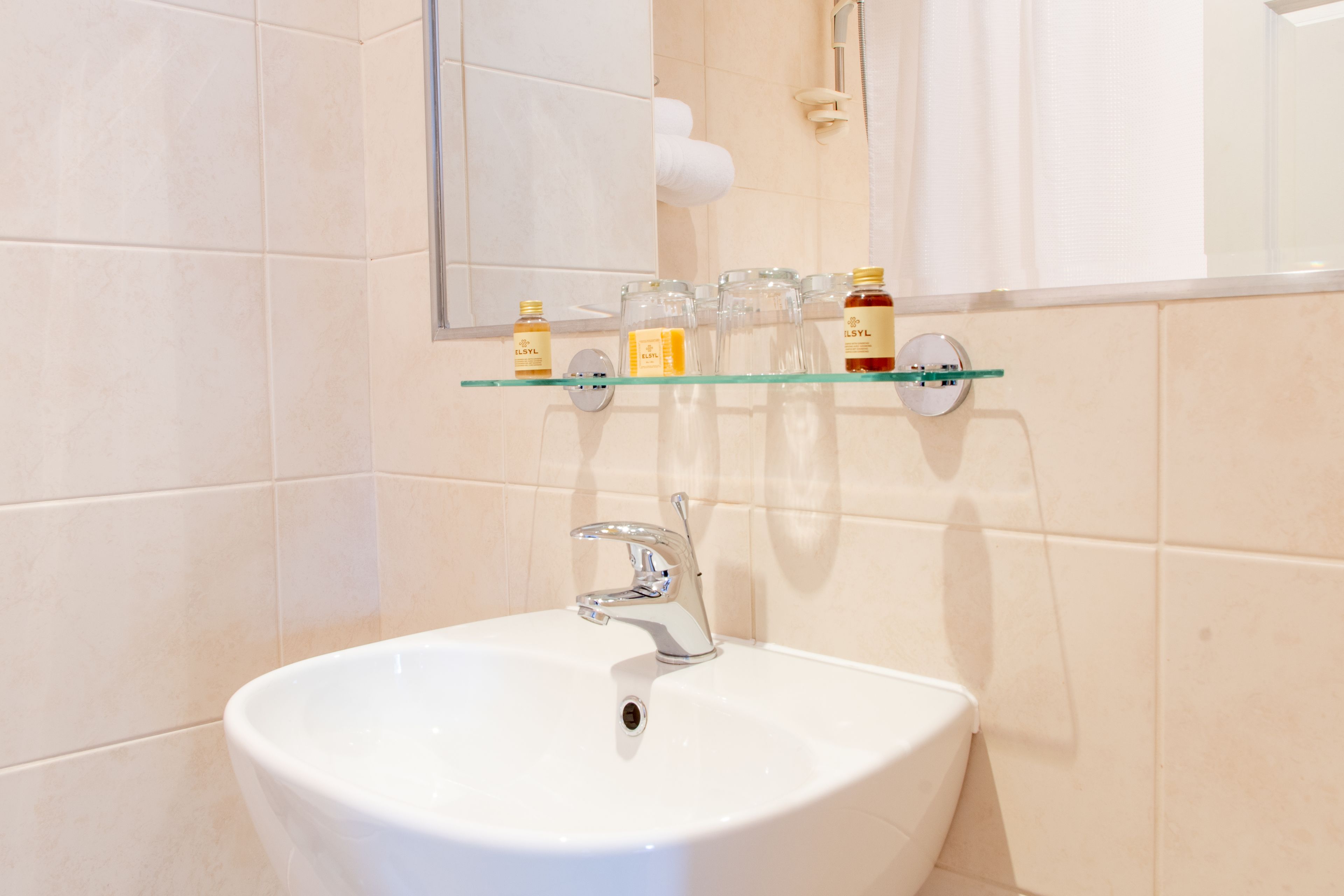 A bathroom with a white sink, a glass shelf with toiletries, and a mirror above the sink.