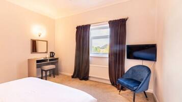 A hotel room with a bed, a desk with a chair, a flat-screen TV mounted on the wall, and a window with curtains.