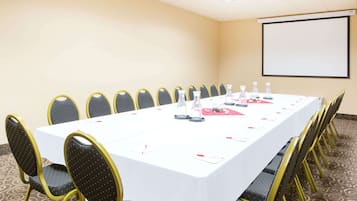 Un salón de conferencias con una larga mesa, sillas y una pantalla de proyector.