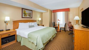 A hotel room with a large bed, a desk with a chair, a television, and a small table with a lamp. - Ramada Tropics Resort & Conf Center by Wyndham Des Moines (Urbandale)