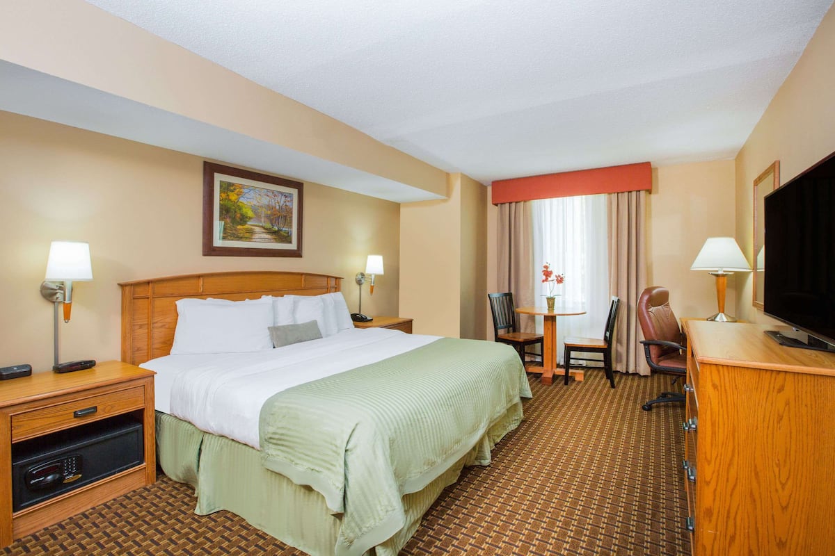 A hotel room with a large bed, a desk with a chair, a television, and a small table with a lamp.