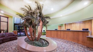 A lobby with a reception desk, a curved seating area, and a decorative palm tree centerpiece. - Ramada Tropics Resort & Conf Center by Wyndham Des Moines (Urbandale)
