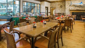 A spacious restaurant with wooden tables and chairs, a stone wall, and a large window overlooking the dining area. - Ramada Tropics Resort & Conf Center by Wyndham Des Moines (Urbandale)