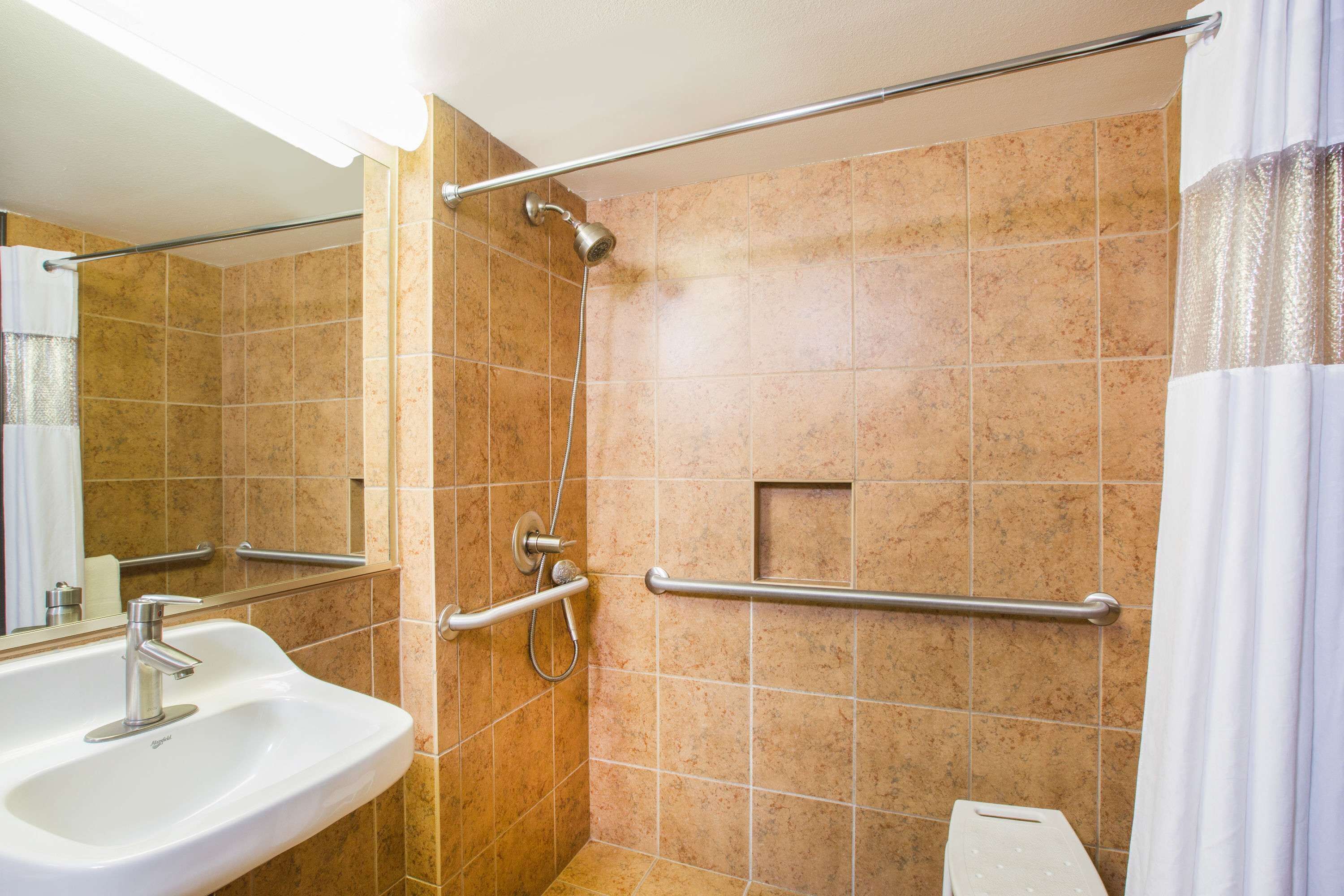 A bathroom with a sink, a shower with a handheld showerhead, and a grab bar.