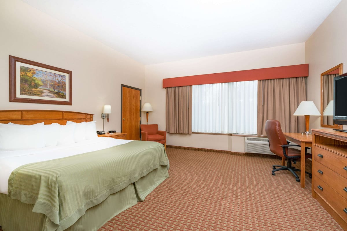 A hotel room with a large bed, a desk with a chair, a television, and a window with curtains.