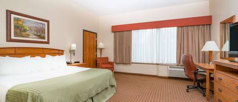A hotel room with a large bed, a desk with a chair, a television, and a window with curtains.
