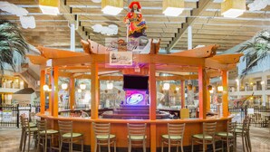 A bar area with a central counter, multiple bar stools, and a decorative figure on top. - Ramada Tropics Resort & Conf Center by Wyndham Des Moines (Urbandale)