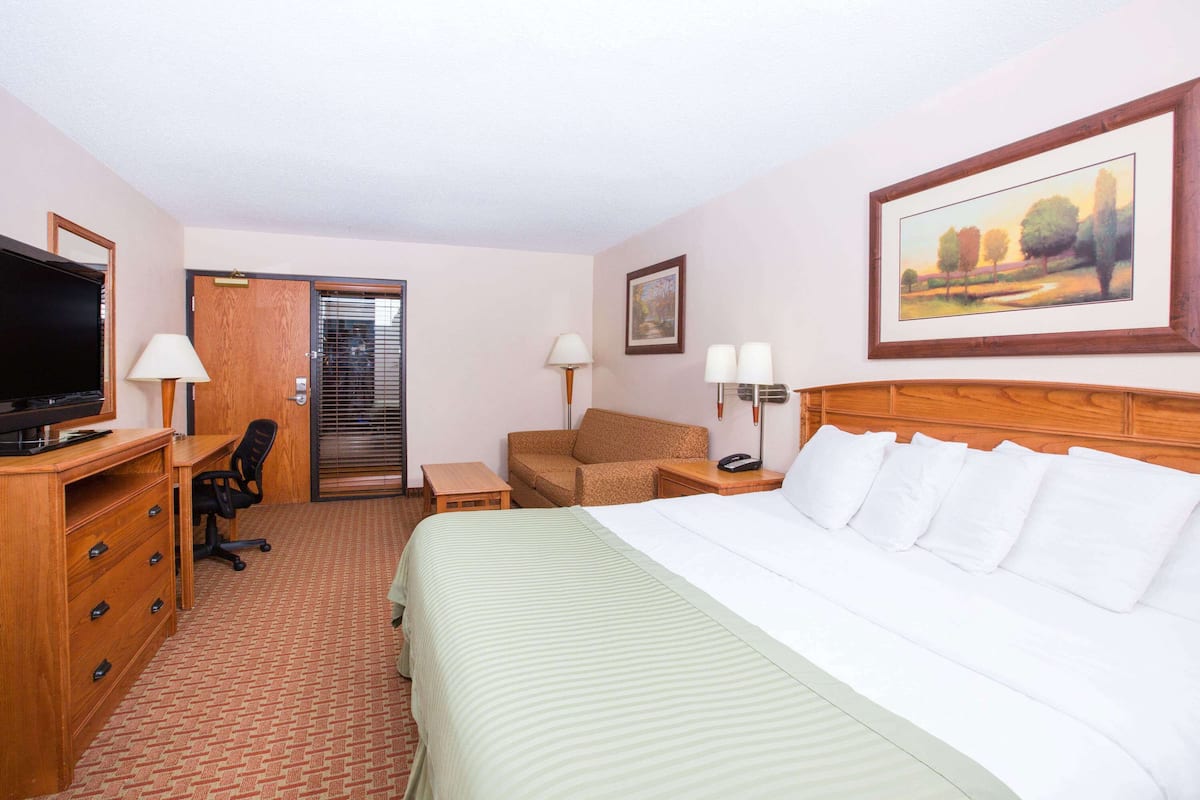 A hotel room with a bed, desk, chair, TV, and a painting on the wall.
