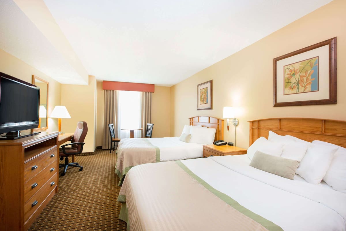 A hotel room with two beds, a desk, a TV, and a chair.
