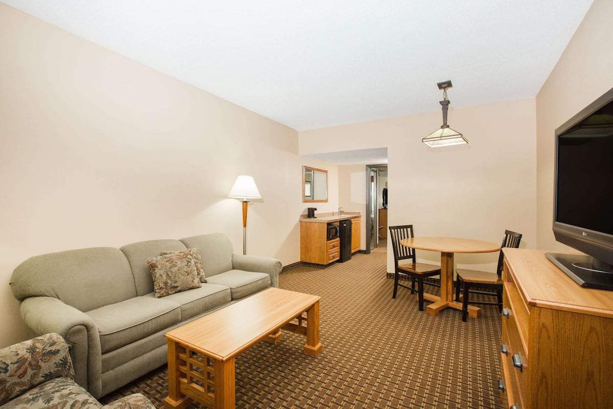 A compact living room with a sofa, a small table, a TV, and a kitchenette in the background.