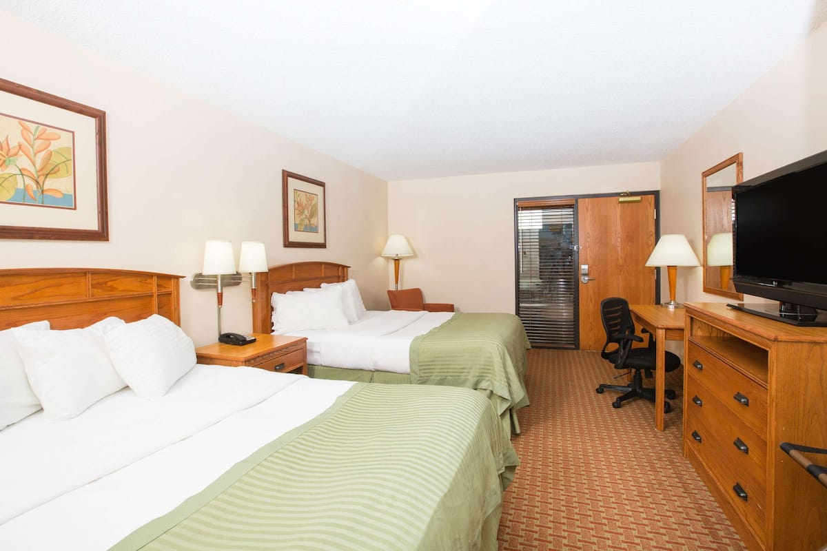 A hotel room with two beds, a desk, a chair, a television, and a wardrobe.