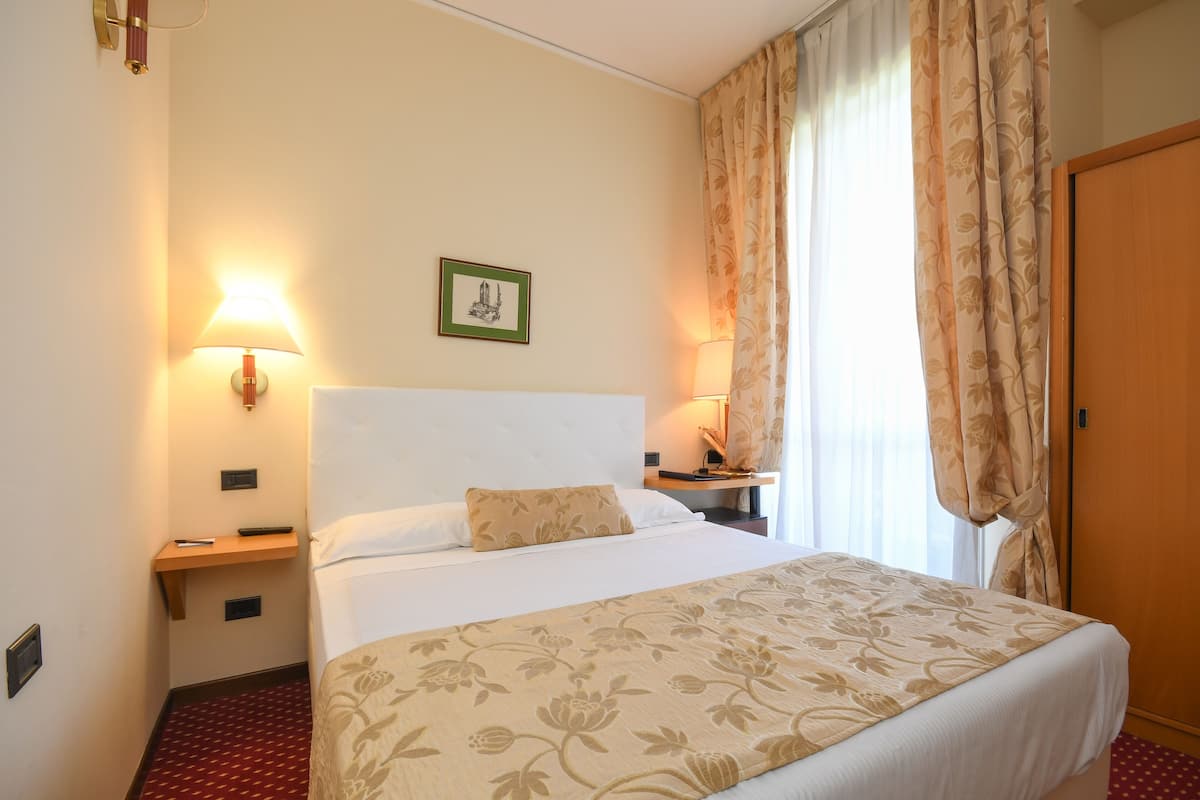 A hotel room with a large bed, two bedside lamps, a nightstand, a wooden door, and a framed picture on the wall.
