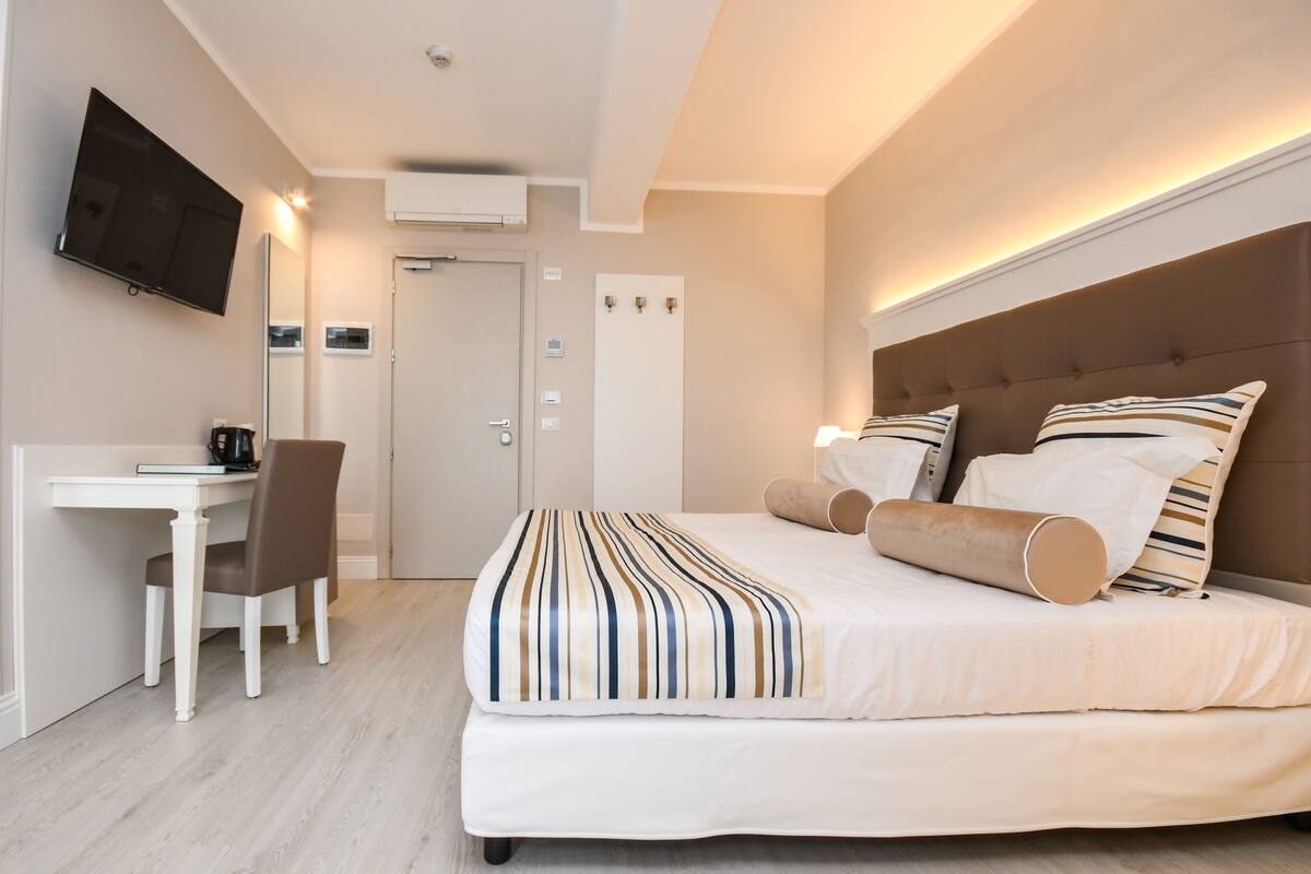 A hotel room with a bed, a desk, a chair, a television, and a door.