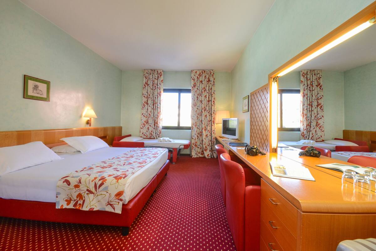 A hotel room with two beds, a desk, a chair, a mirror, and a TV.