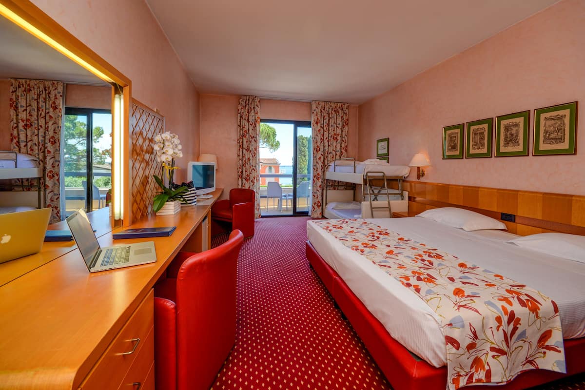 A hotel room with a bed, desk, chair, laptop, and a view of the outdoors.