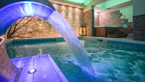 Una piscina con una cascada, paredes de piedra y una zona con bancos de madera.