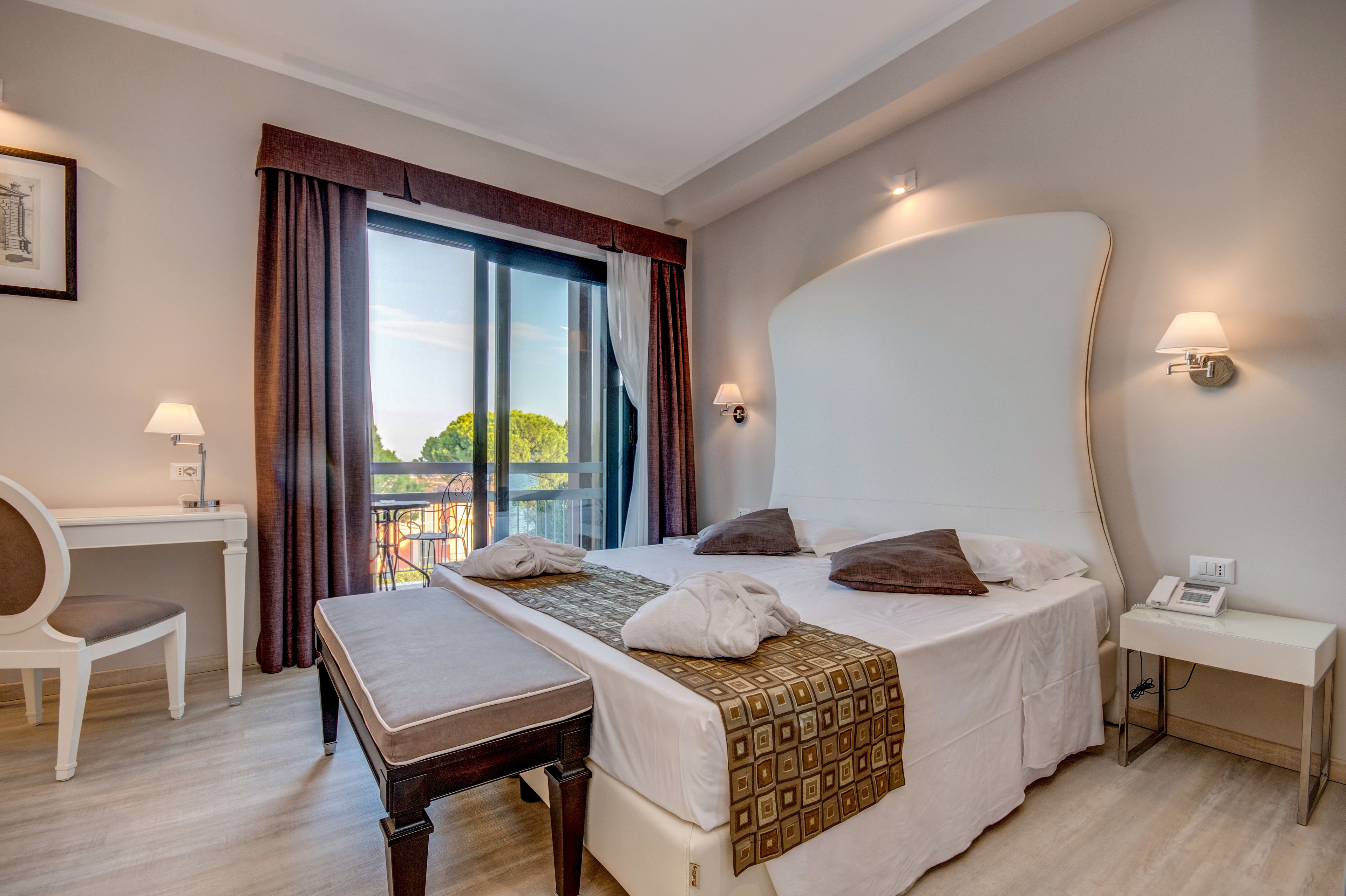 Quarto de hotel com uma cama grande, uma mesa, uma cadeira e vista para o exterior.