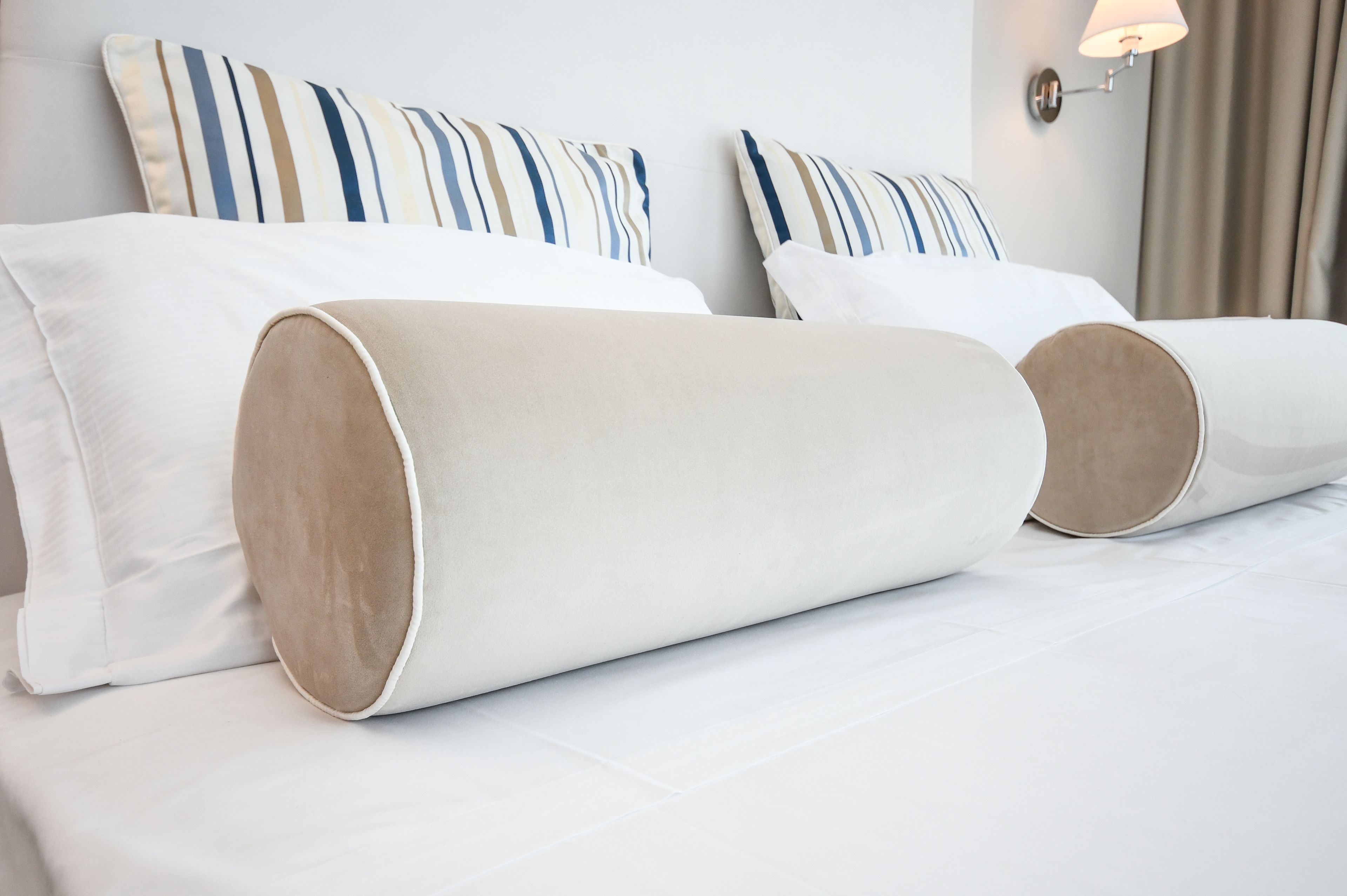 A neatly made bed with white linens and two cylindrical pillows.
